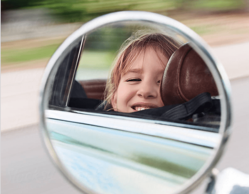 Mirror image of kid looking out car window with blurry background.