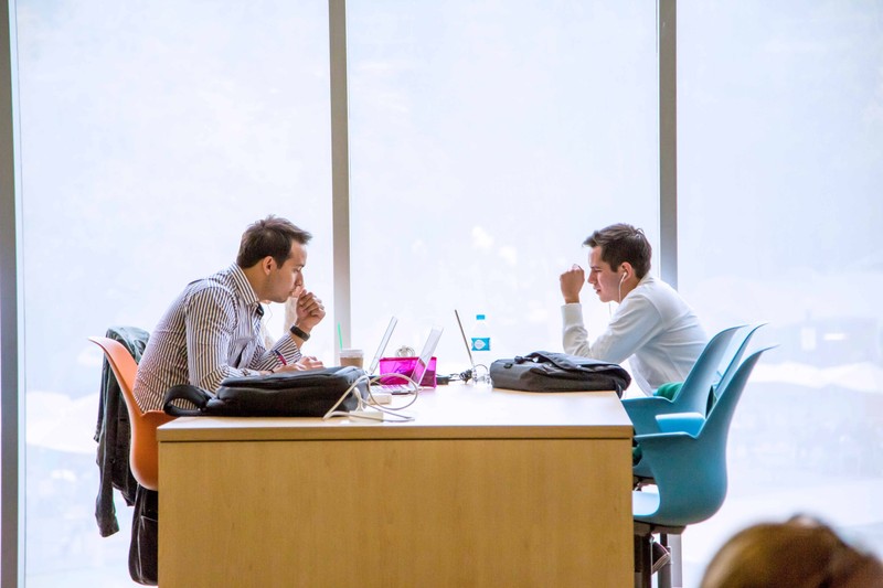 Two EGADE Business School students studying on their laptops next to a big, bright window