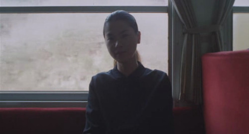 A screenshot of a woman with her hair in a ponytail sitting on an old passenger train. From the film 'Maborosi'.