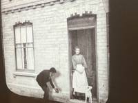 photo of woman standing in her doorway with a dog. Man bending down to feed the dog.