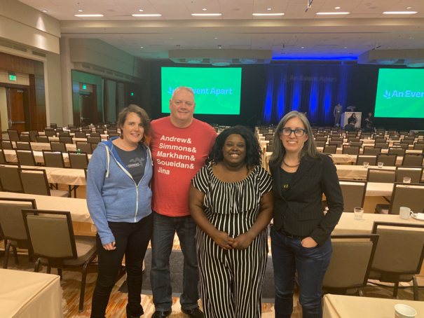 Miriam Suzanne, Todd Libby, Mina Markham, and Jen Simmons standing in the conference hall at An Event Apart Denver. Todd has his red Andrew& Simmons& Markham& Soueidan& Jina shirt on.
