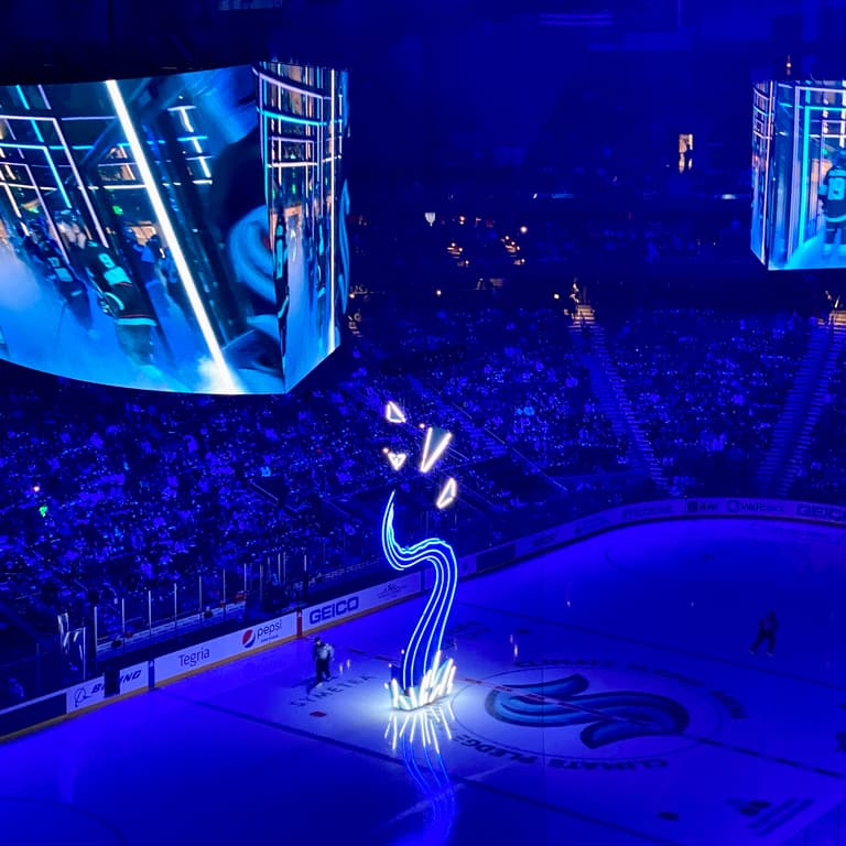 A hockey arena lit by blue ambient light, with a neon sculpture that looks both like an S and kraken tentacle