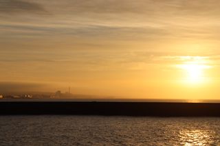 Sun rising over a harbour wall with a golden mist reflecting onto the coastline.