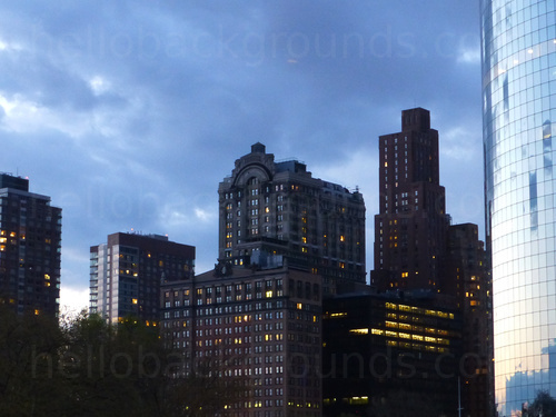 Evening urban cityscape featuring multiple tall office buildings bearing many windows in front of cloudy sky Zoom background