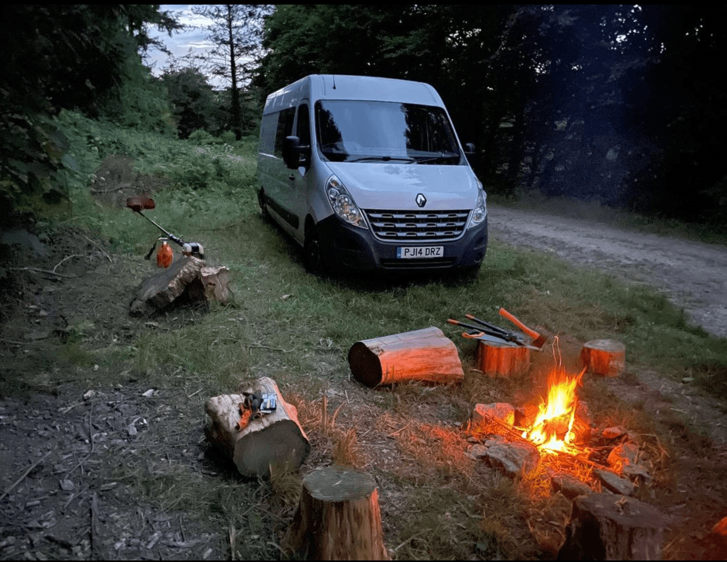 Large rental camper van in the woods, with a fire circle.