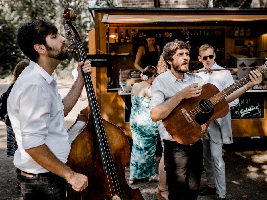 Zwei Musikanten machen Live Musik bei einer Hochzeit vor einem schönen Crêpestand mit Holzoptik