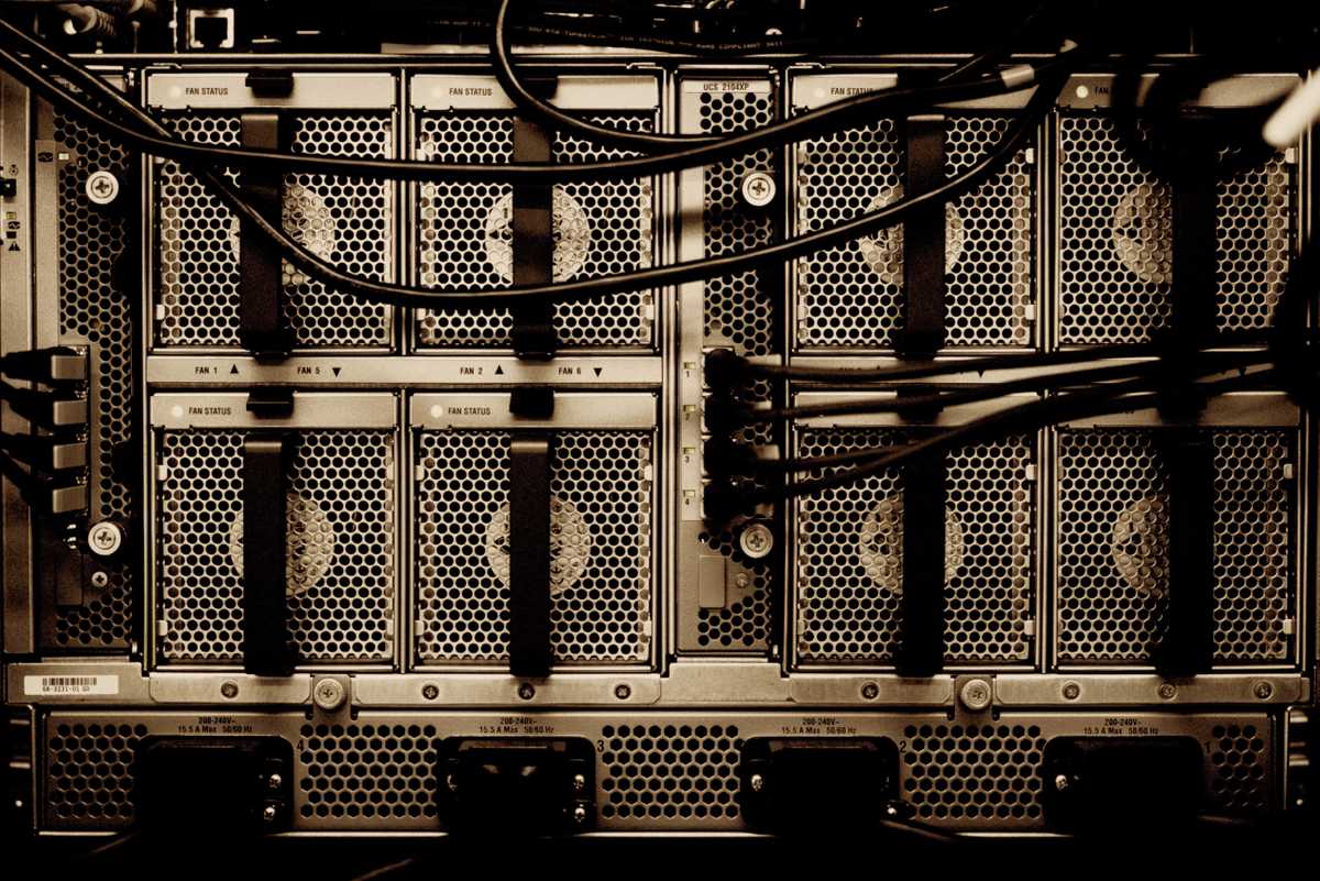 Tangled power and data wires emerge from the rear ports of a server, installed in its rack.