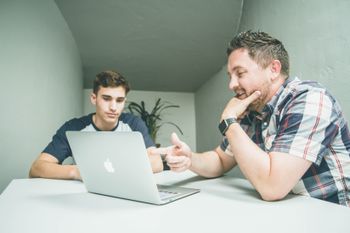 A person talking and mentoring another person on table with laptop on top of it