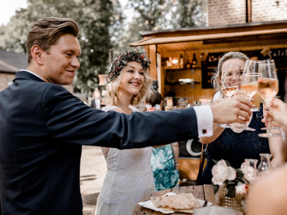 Hochzeitspaar stößt über einem Crêpe mit Hochzeitsgästen vor dem Hintergrund eines gemütlichen Crepestandes an