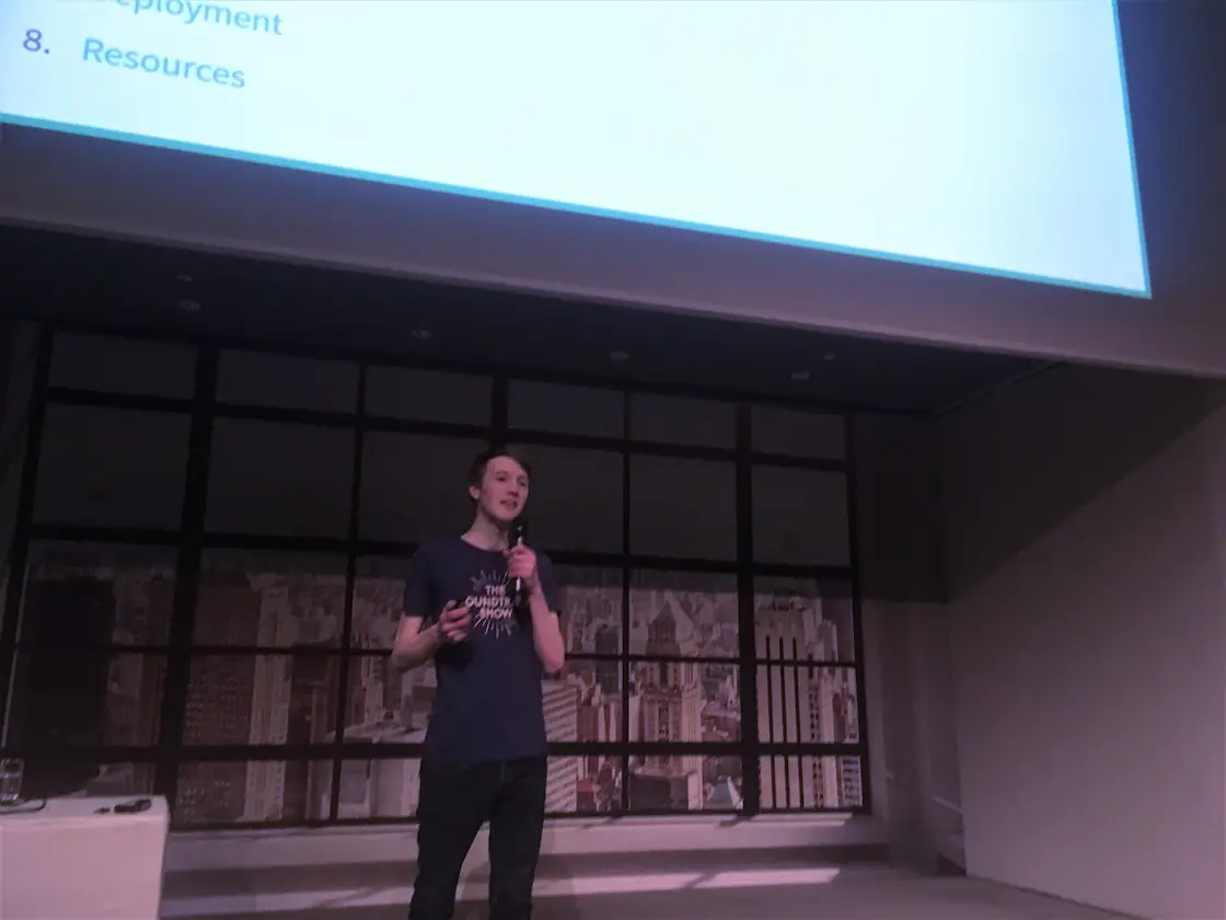 Fynn Becker holding a microphone standing under a giant screen with the slides from his Nuxt.js talk.