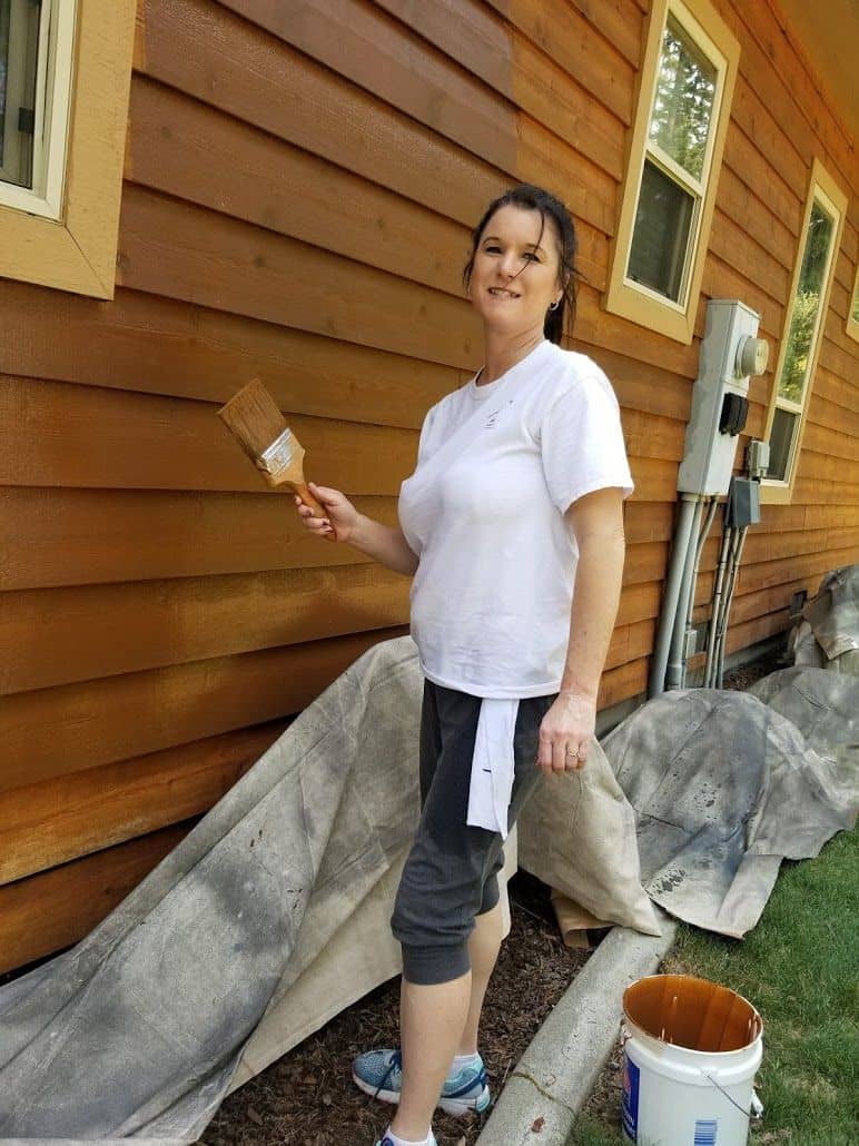 enlarged photo of woman painting the side of a wooden siding home