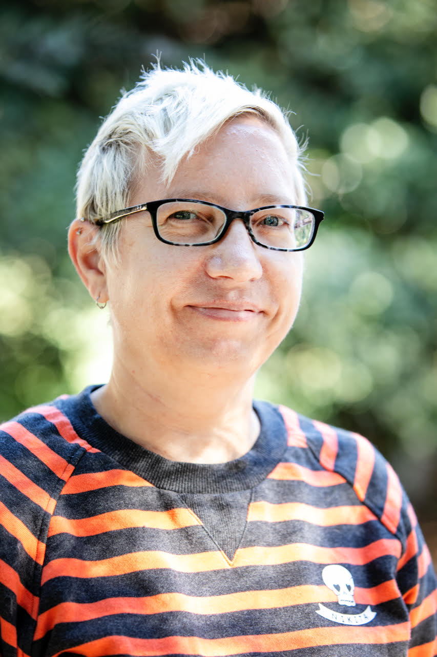 color photo headshot of a woman with a blonde pixie haircut wearing a striped tshirt and glasses