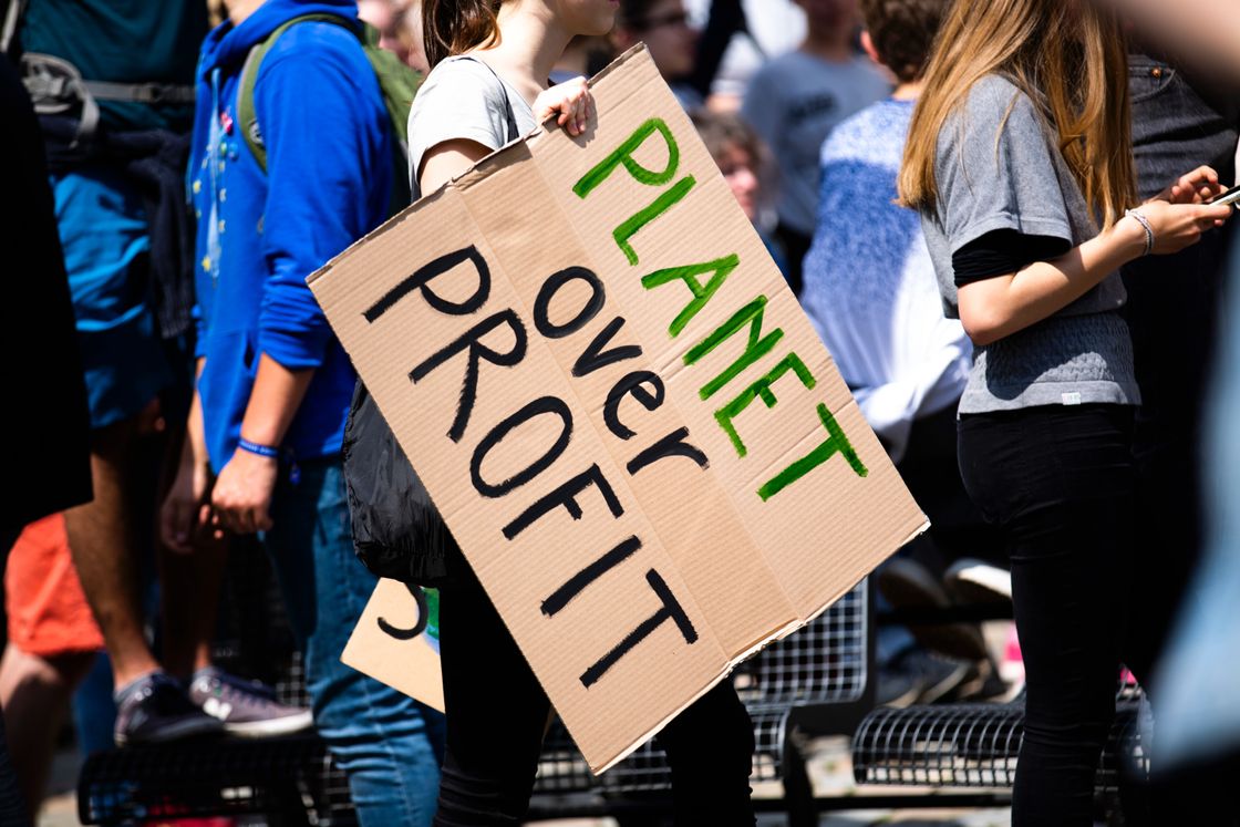 Group of eco protestors, one holding a paper sign reading “Planet over Profit”.