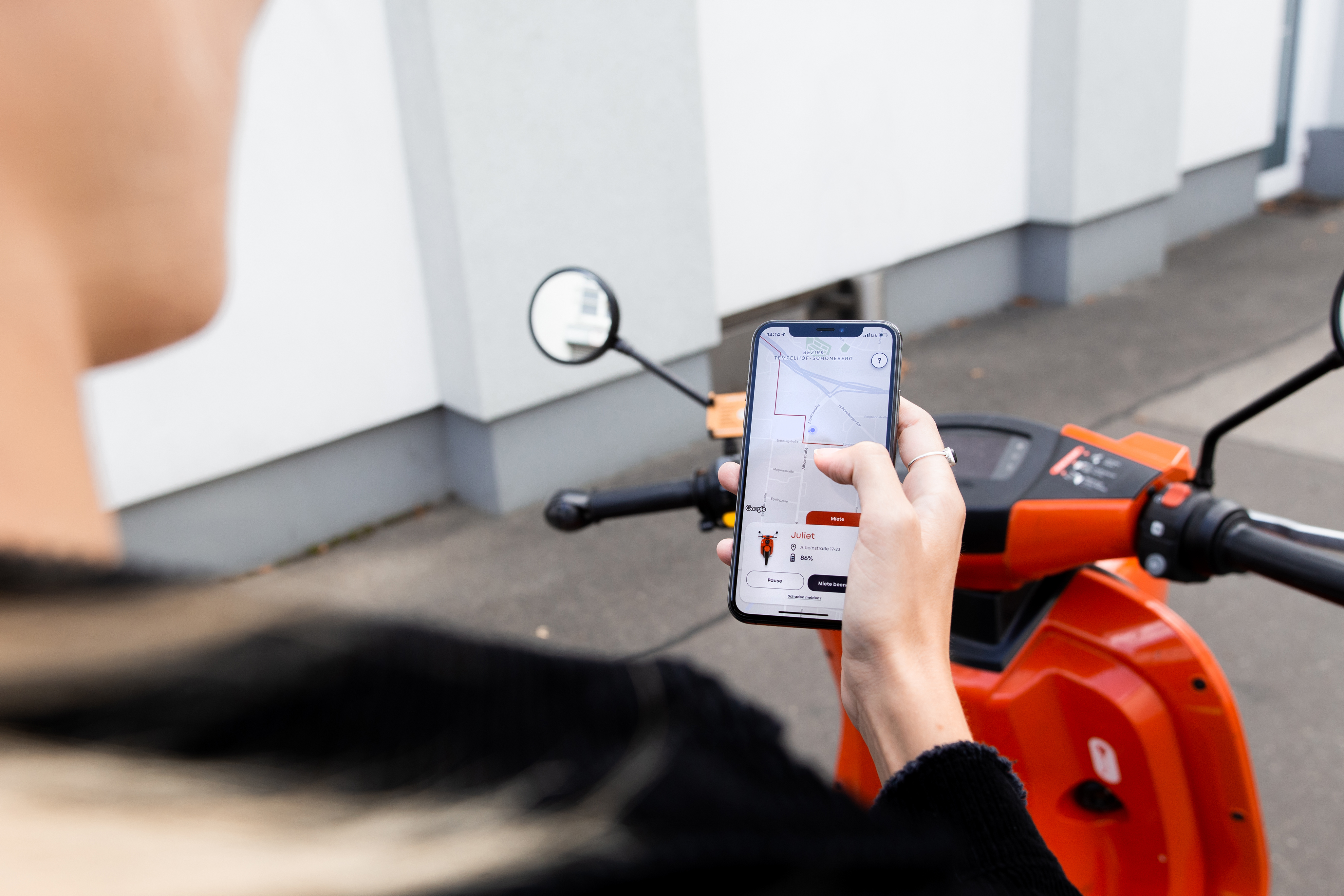 emmy customer card of a caucasian female person holding a mobile phone with Wunder Mobility app on while sitting on emmy moped in the street.