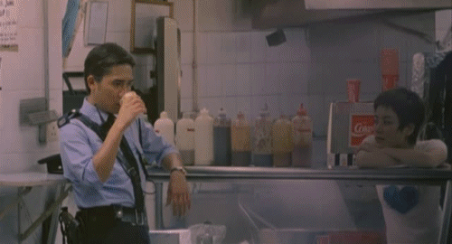 An animated gif of a scene from the film 'Chungking Express' of a police officer drinking coffee at a standing coffee shop as people pass by.