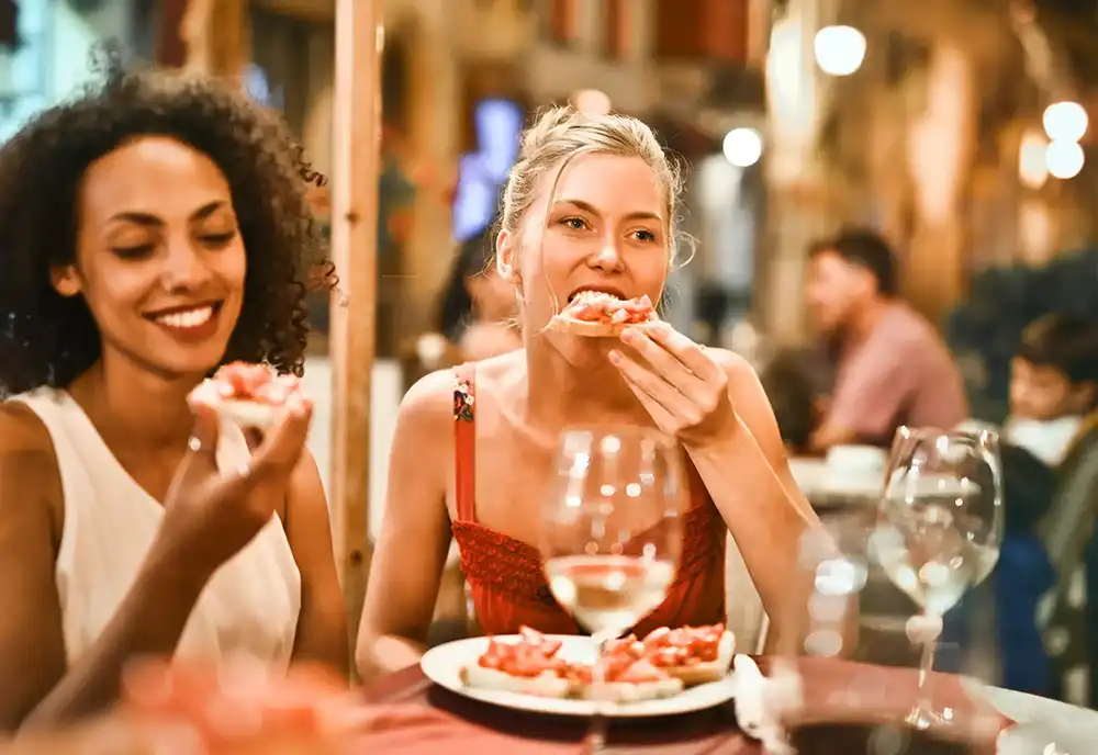 Two young women enjoying pizza and wine