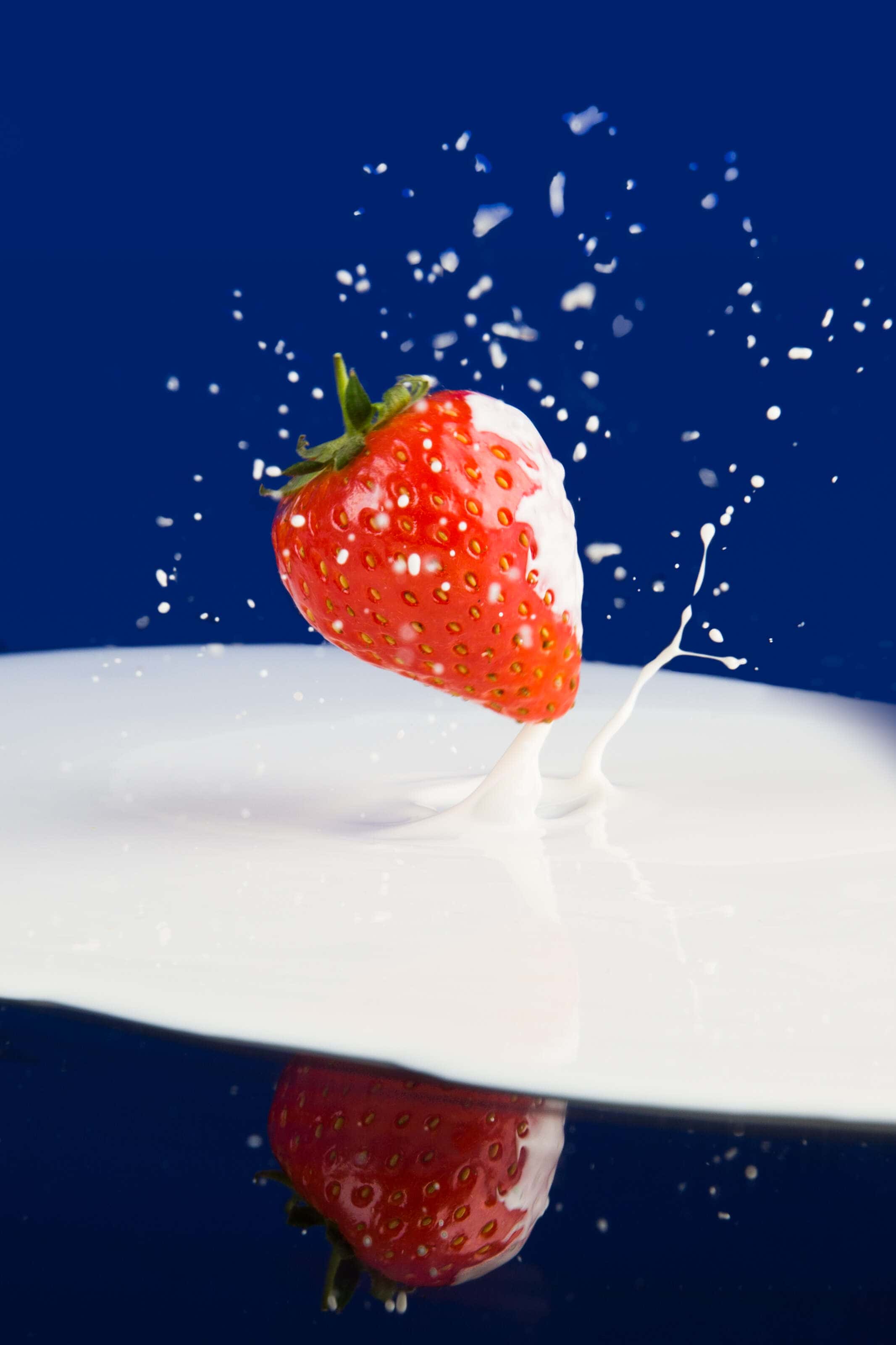 A strawbery falling onto cream on a mirrored surface.