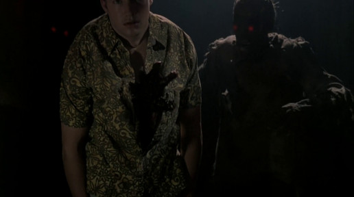 A man in a floral print shirt stands with a bloddied hand coming out of his chest. There are two "zombies" behind him, with glowing red eyes.
