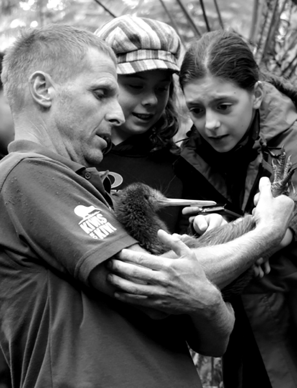 Man holding a kiwi with children looking on