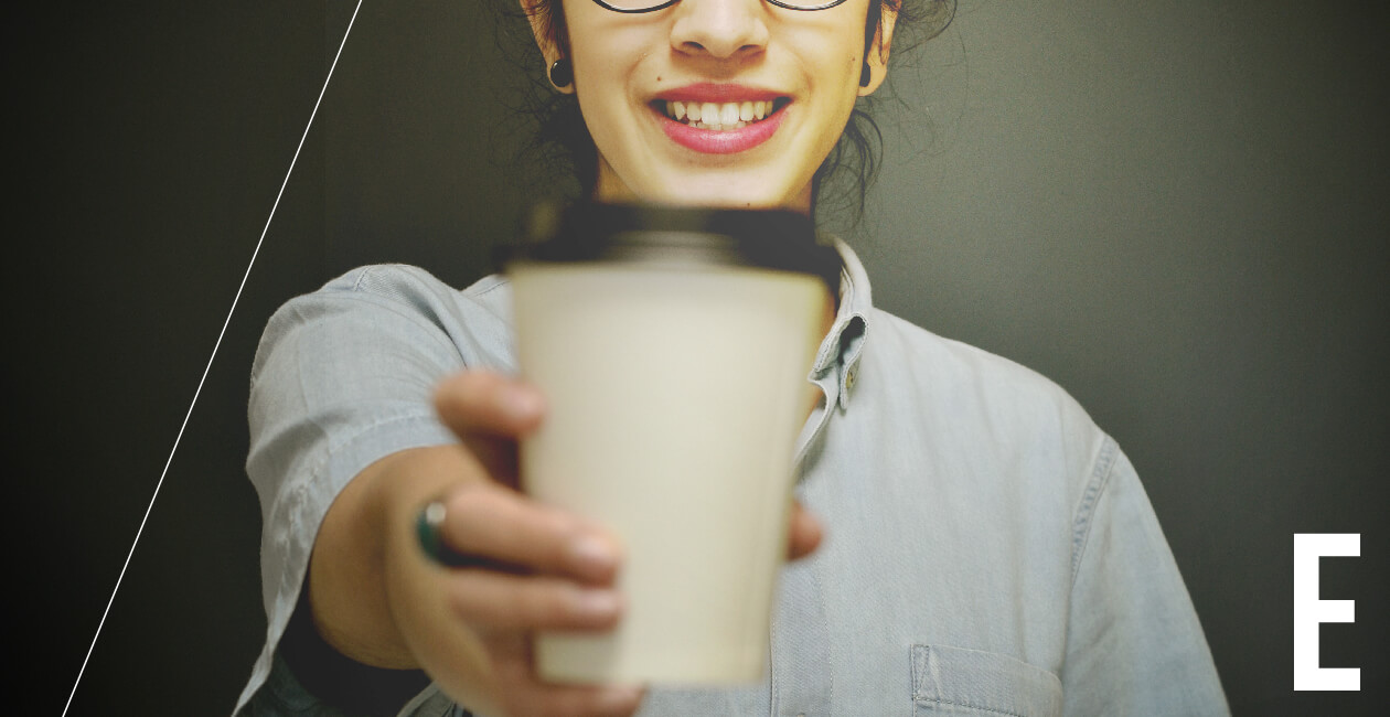 Empathetic woman UX designer holding a cup of coffee Empathetic woman UX designer holding a cup of coffee out to the camera and smiling
