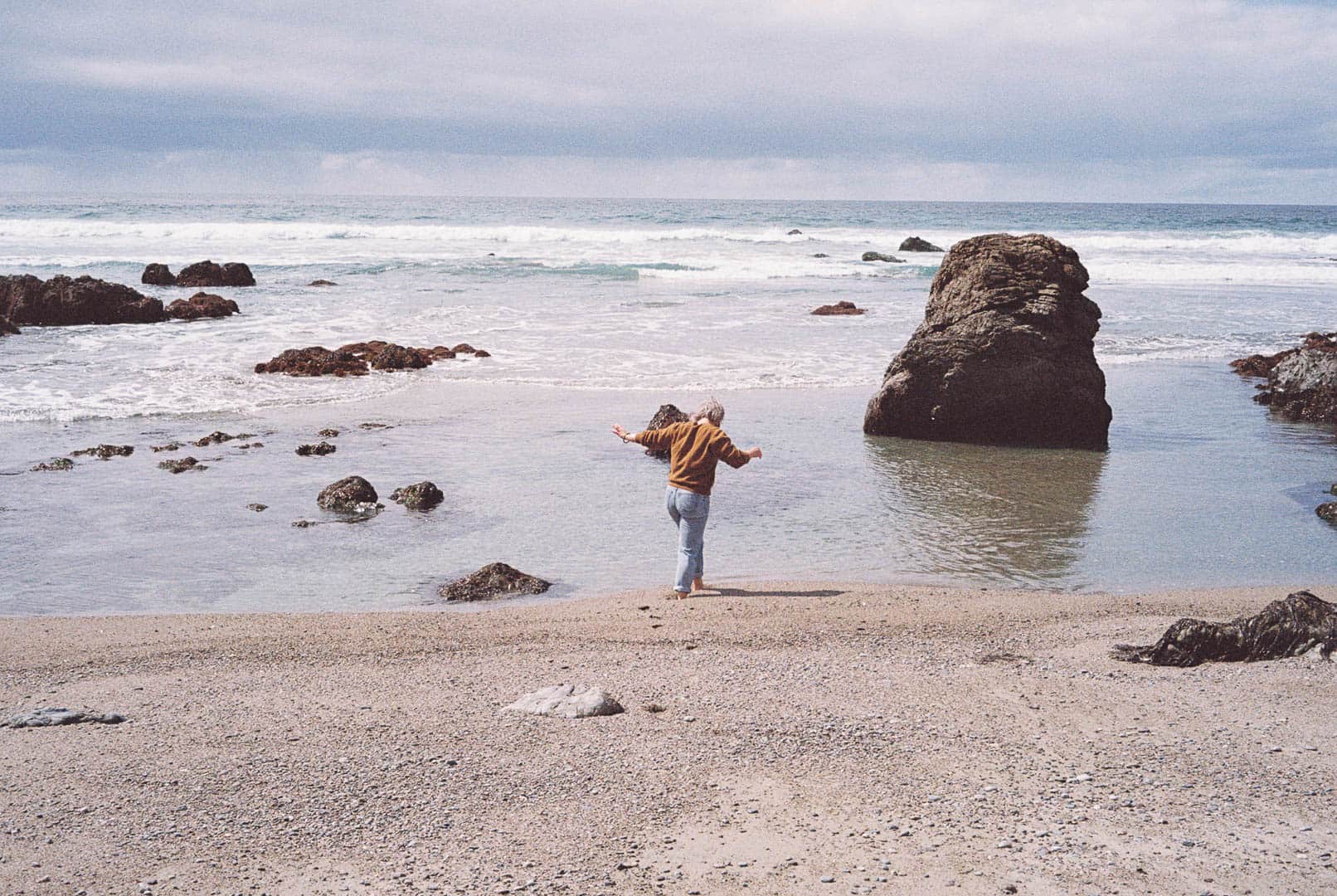 A woman walking into the water of a rocky beach