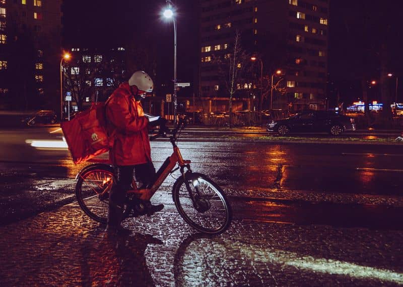 Mobiles Arbeiten, Kuriere und Fahrer:innen Ein Kurier, der Essen mit einem Rad ausliefert und auf sein Handy schaut