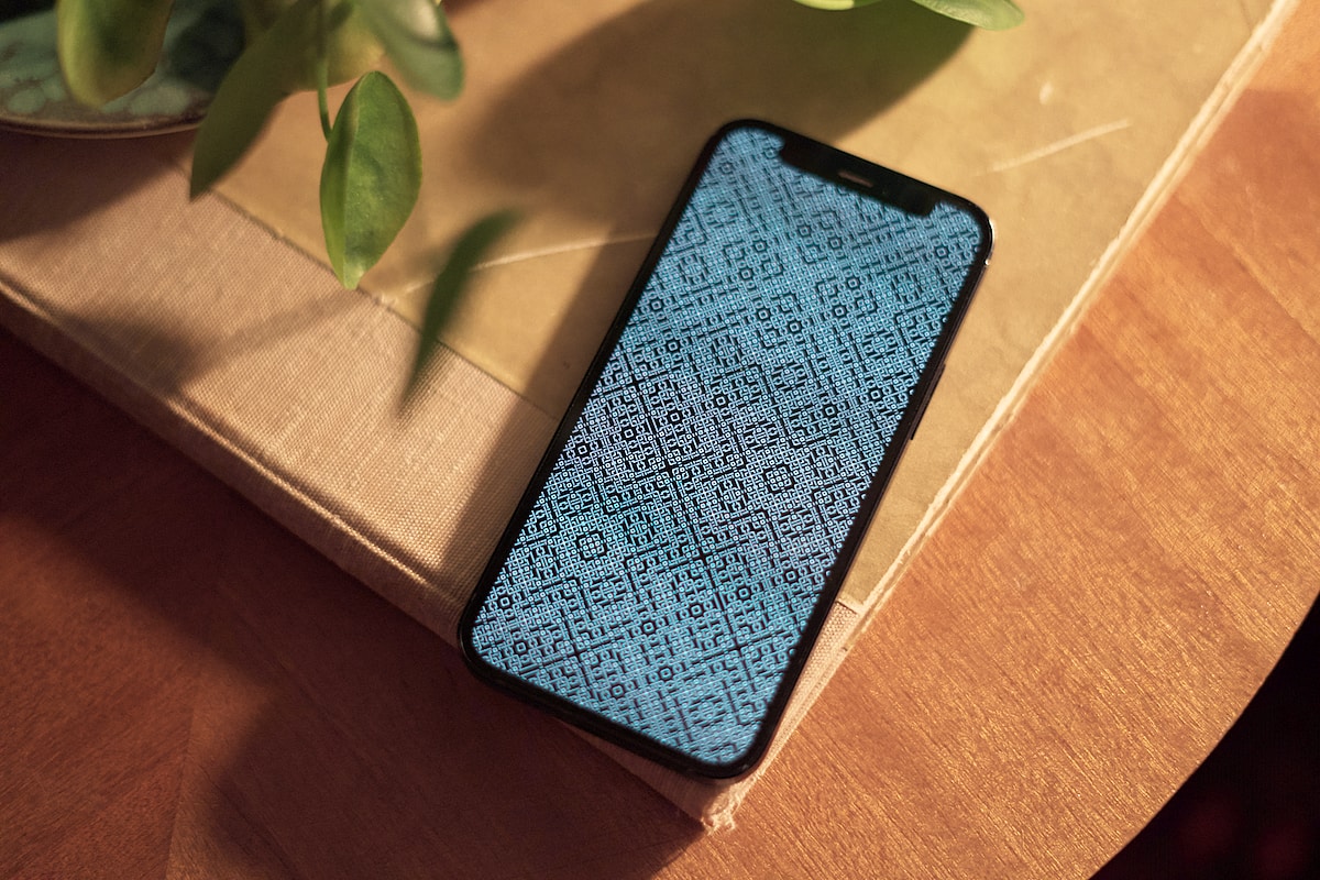 A phone on a table displays a full-screen black and white complex but beautiful pixel pattern.
