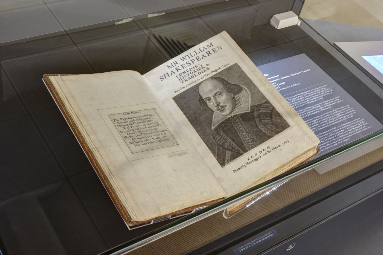A photo showing the FIrst Folio. The folio is opened up to a black and white etching of Shakesphere's portrait.