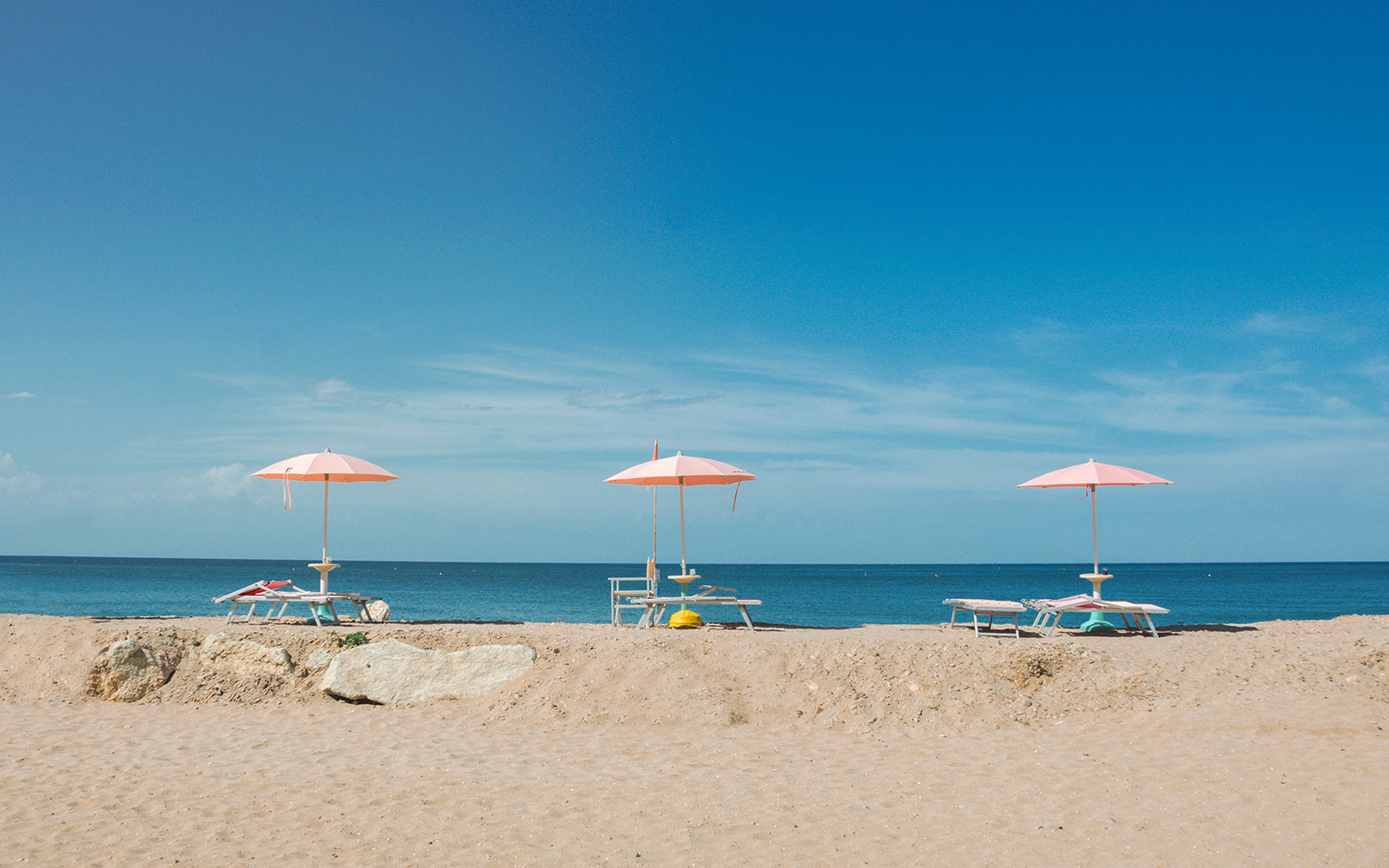 three pink sun umbrellas lined up on the beach