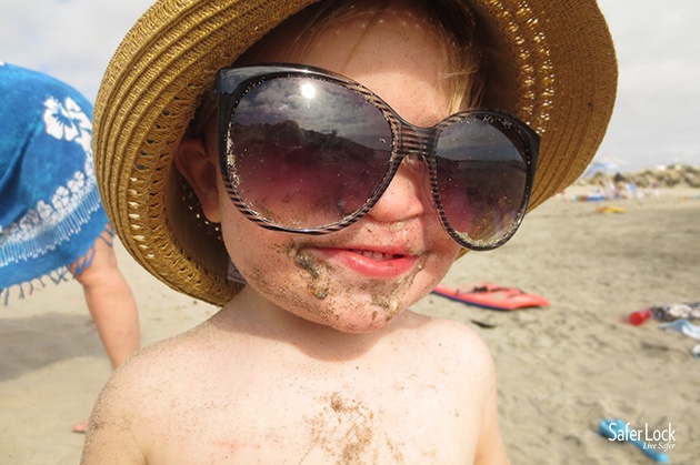 Baby at the beach wearing large sunglasses and a hat.