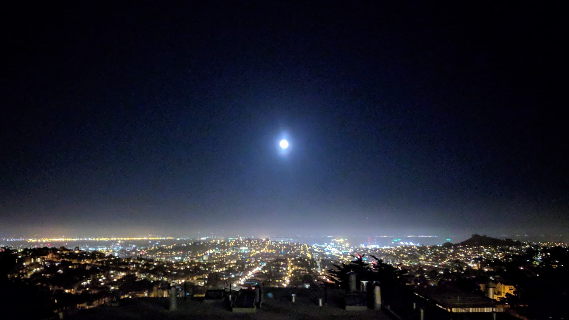 Looking east across San Francisco at night. The Moon is high in the sky, and the other side of San Francisco Bay can just be seen on the horizon.