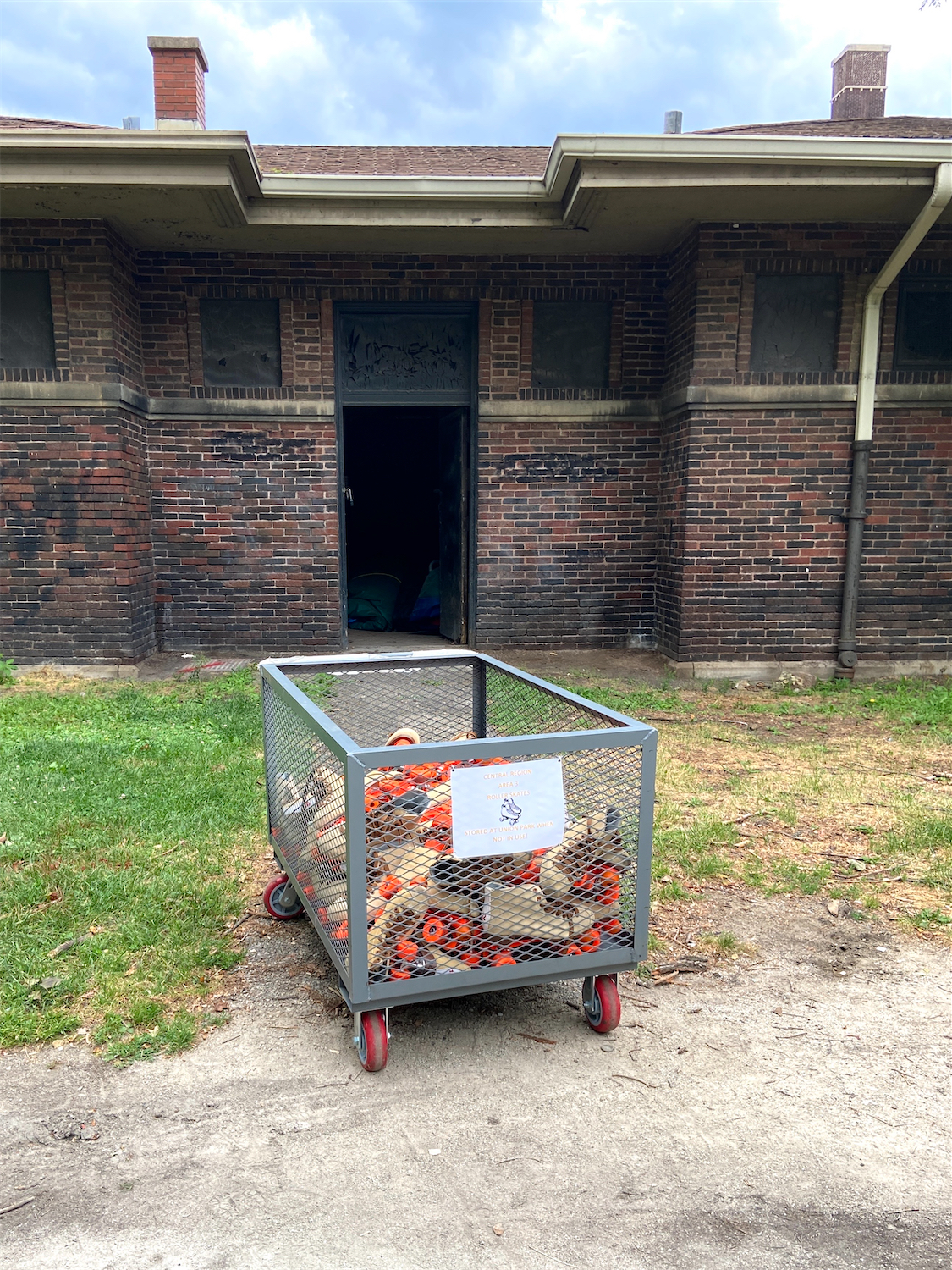 A metal cart full of old school roller skates with bright orange wheels, in front of an old brick field house at Union Park in Chicago.