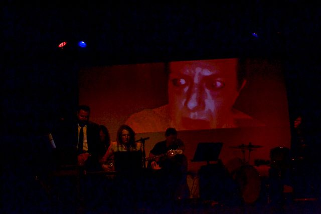 Jane's concerned face
in a red glow,
projected from her hiding place
onto a screen behind the band.
