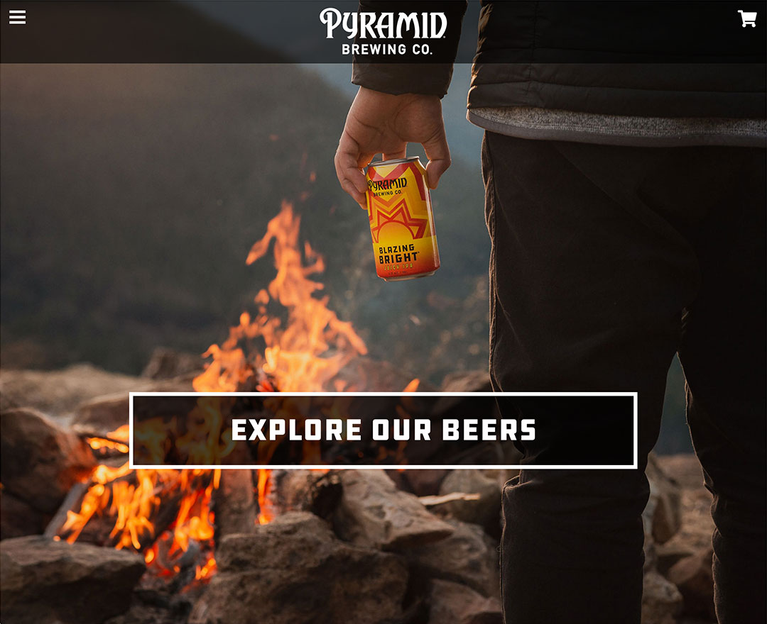 Screenshot of the Pyramid Brewing Co. website with a photo of a man from behind holding a can of beer with a campfire in the background.