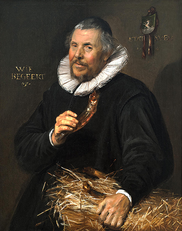 Portrait of older man holding a dried herring. His other hand rests on a bale of hay.