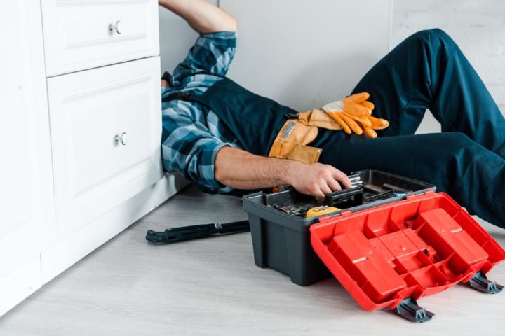 plumber working in kitchen near toolbox while lying on floor