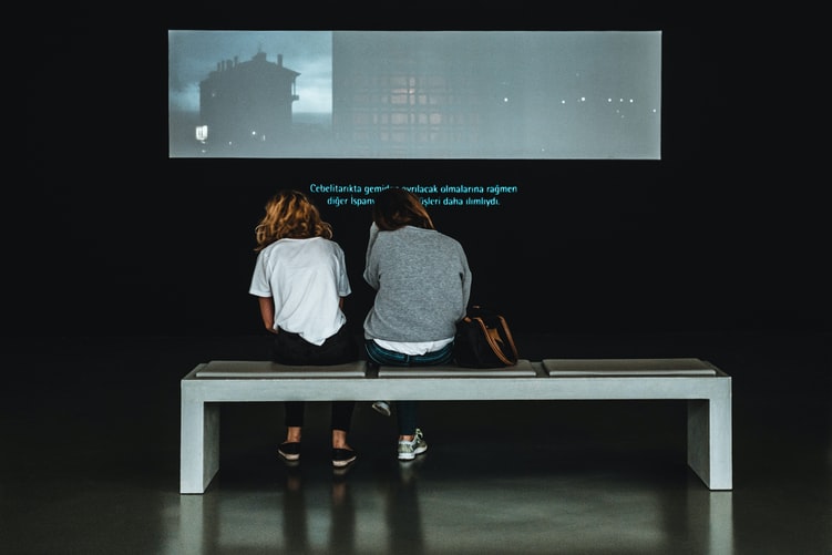 Two people sitting on bench and watching a TV program or movie with subtitles