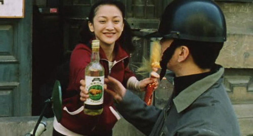 A screenshot of a young woman in a red jumpsuit waving a mermaid doll in the face of her motorcycle taxi driver. From the Chinese movie 'Suzhou River'.