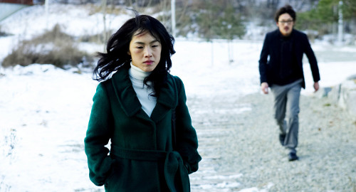 A screenshot of Yeon walking towards the camera in the snow as the blurry figure of a man pursues her. From the movie 'Breath'.