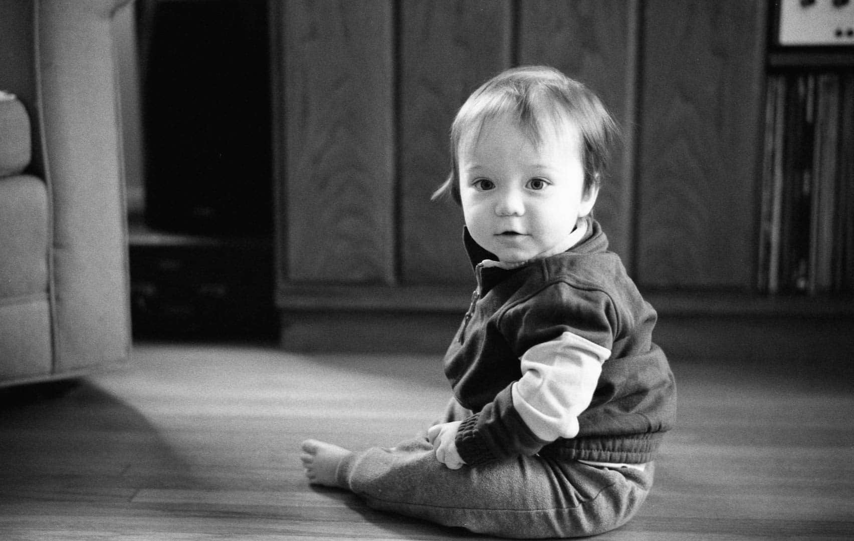 A baby sitting in a living room looking into the camera
