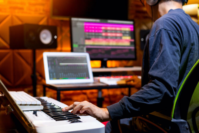 persona en un estudio con piano digital de 88 teclas en soporte y macbook con pantalla externa en escritorio