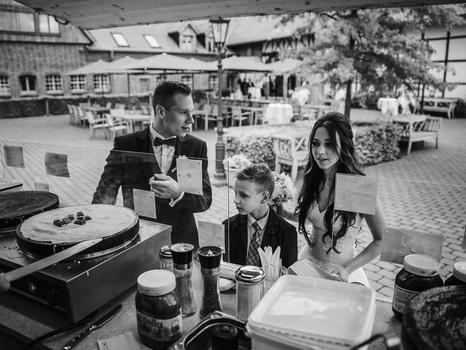 Brautpaar mit einem Kind schaut voller Vorfreude bei der Zubereitung eines Crêpe mit Kinderriegel zu