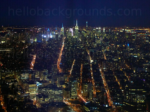 Aerial view of urban cityscape at night featuring distant skyscraper buildings and many illuminated windows and lights Google Meet background