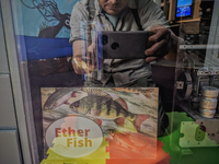 A floating goldfish behind a sign saying Ether Fish.  But mostly showing a man reflected! 
