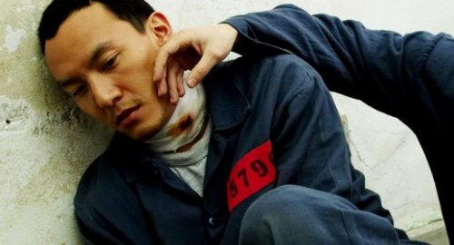 A screenshot from the movie 'Breath' of a young man, Jin, who is a prisoner huddled against the wall to reject the hand that is brushing across his face.