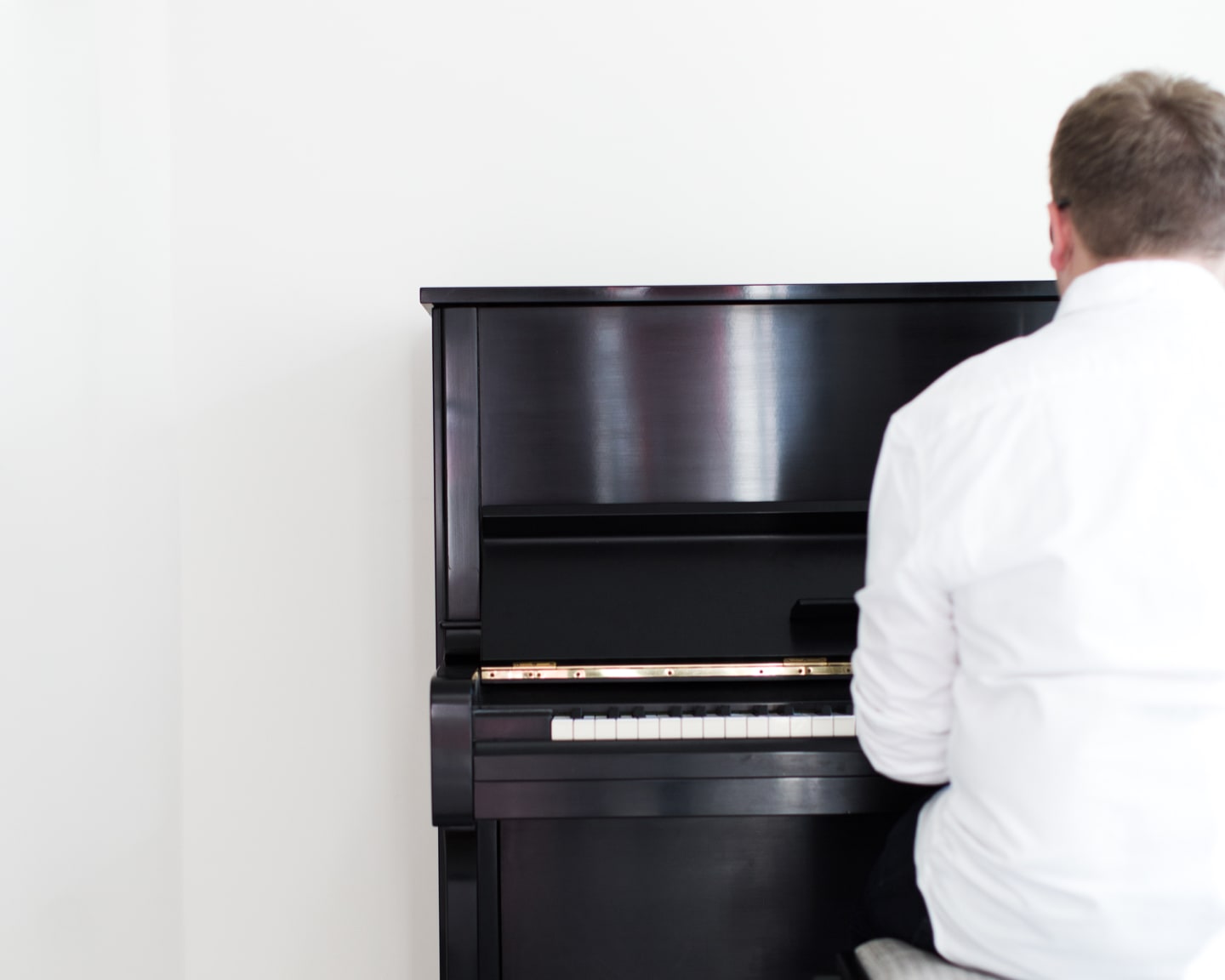 Jack Watkins playing a black Yamaha upright piano in a simple, light filled white space