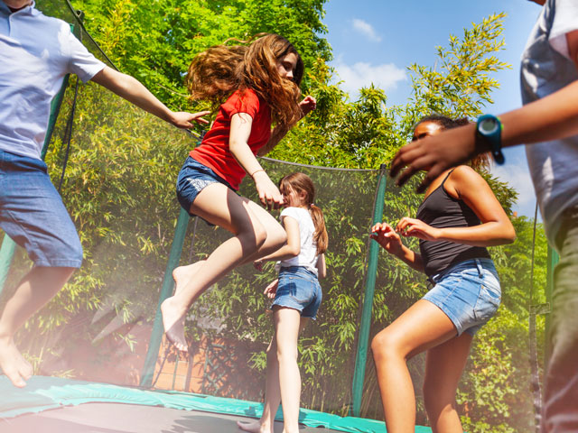 Five teenagers jumping on a trampoline outside and having fun