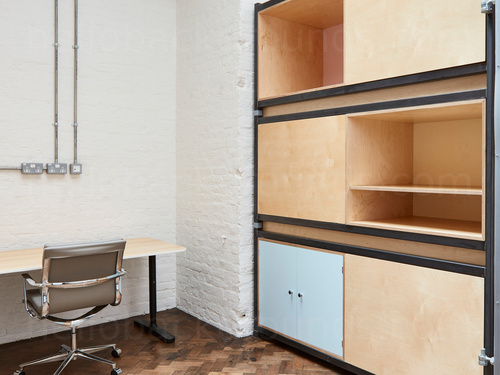 Basic private office featuring wooden shelving unit and desk with metal framed grey chair Zoom background