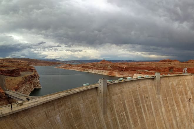 The Glen Canyon Dam, with Lake Powell extending behind it to the horizon. The rocks on either side of the lake are bright red-orange, but turn white just above the water.
