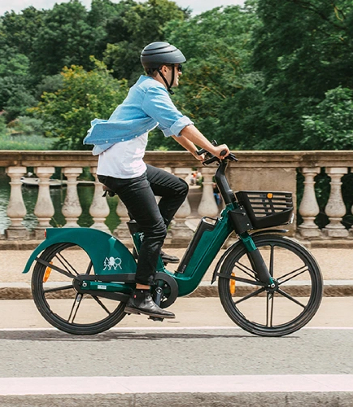 Human Forest customer card image featuring a caucasian man riding an okai e-bike with a helmet on, during a green day in London. 